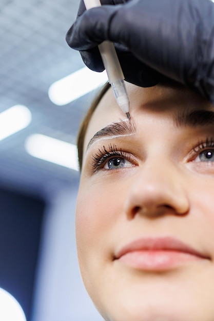 El maestro marca el rostro de la mujer antes del maquillaje permanente de cejas Tatuaje de cejas Procedimiento de belleza para el rostro de una mujer