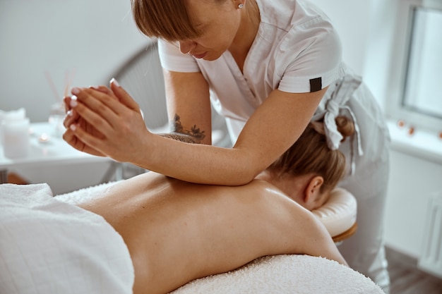 El maestro de masajes confiado profesional está realizando procedimientos para una mujer caucásica en un moderno minimalista