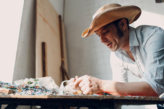 El maestro de mosaicos de hombre elige piezas de vidrio esmaltadas seleccionadas para el panel de mosaico Mosaico masculino en el trabajo