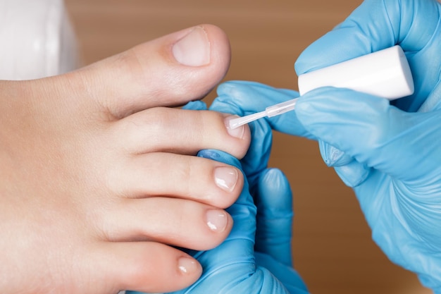 El maestro de pedicura aplica esmalte de uñas incoloro.