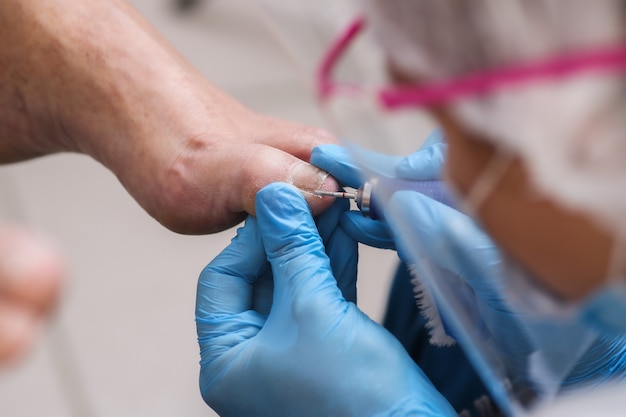 Maestro de pedicura en máscara y gafas, pule las uñas de los pies