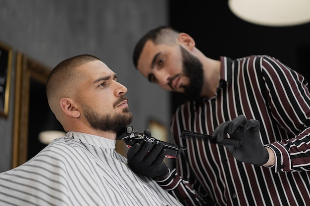 El maestro peluquero de apariencia caucásica hace su trabajo cortando la barba y el cabello en la cabeza