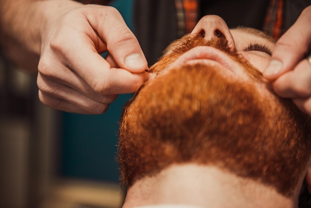 Foto el maestro peluquero profesional corta la barba del cliente.