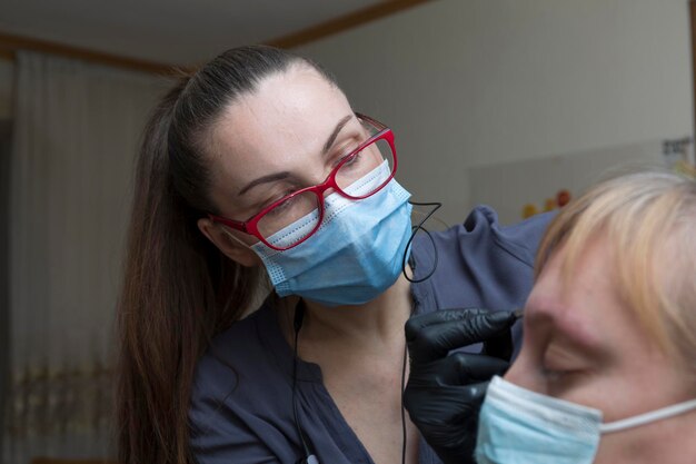 El maestro pinta las cejas de un cliente en casa durante una pandemia, las personas se comunican con máscaras protectoras