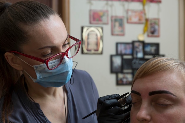 El maestro pinta las cejas de un cliente en casa durante una pandemia, las personas se comunican con máscaras protectoras