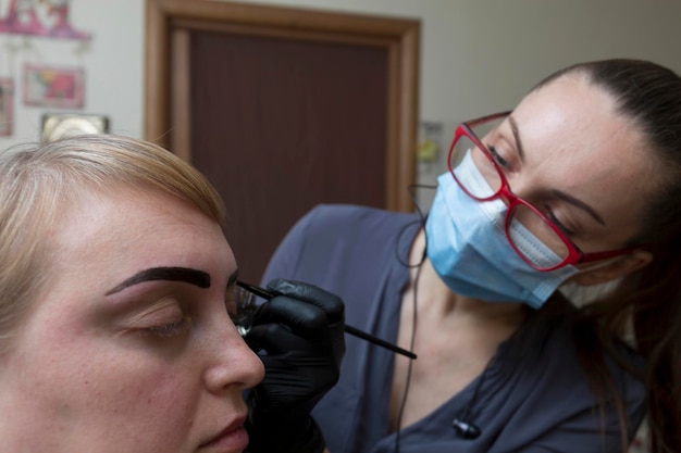 El maestro pinta las cejas de un cliente en casa durante una pandemia, las personas se comunican con máscaras protectoras