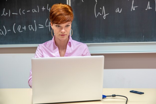 Un maestro de secundaria escribe tareas para estudiantes en su computadora portátil blanca