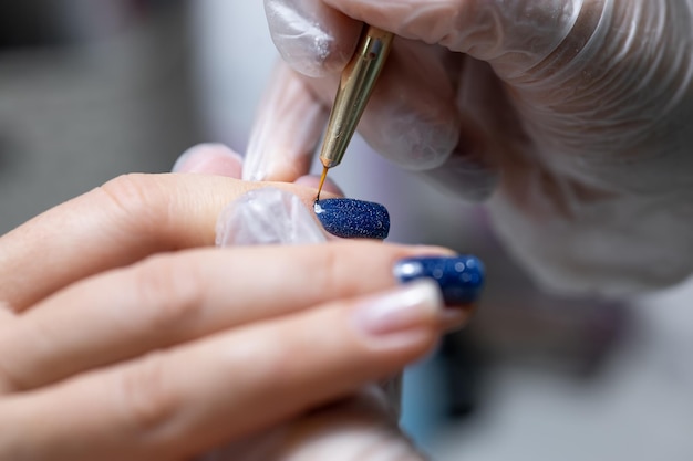 El maestro del servicio de uñas hace una manicura distribuyendo esmalte de gel en la superficie de la uña con un cepillo de uñas fino