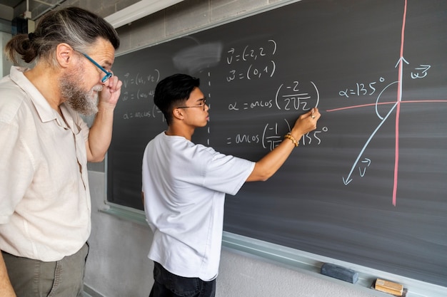 El maestro supervisa a los estudiantes asiáticos de la escuela secundaria escribiendo ejercicios de matemáticas en la pizarra Educación