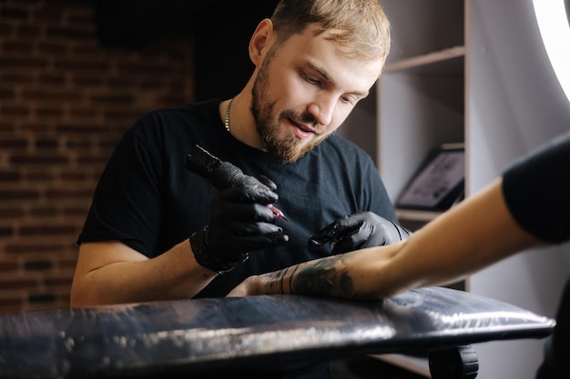 El maestro del tatuaje está tatuando la seguridad e higiene de la máquina de tatuaje inalámbrica de la mano de una mujer en el primer plano del trabajo