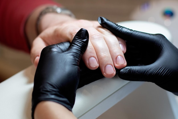Maestro de uñas sosteniendo mano masculina con manicura en salón de belleza
