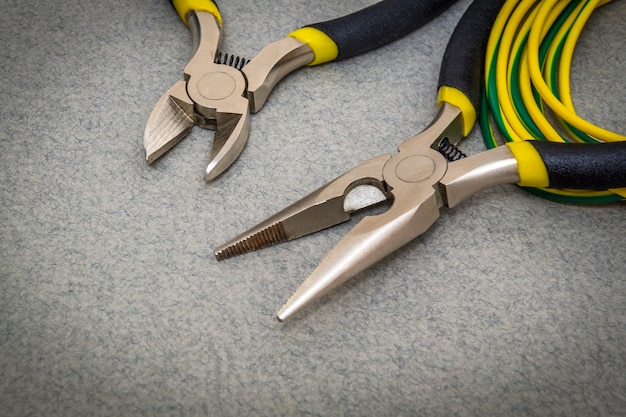 El maestro utiliza dos alicates y cables para un electricista sobre fondo gris para reparar la electricidad