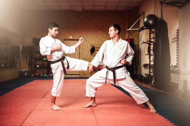 Maestros de artes marciales en kimono blanco y cinturones negros, práctica de autodefensa en gimnasio