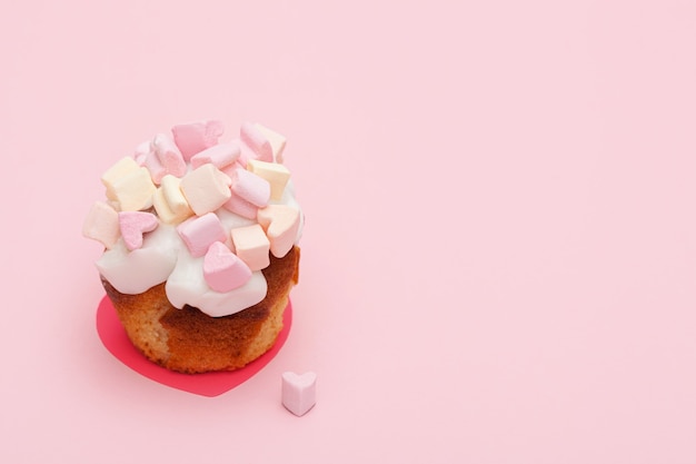 Foto magdalena con corazones de malvavisco sobre un fondo rosa con corazoncito cerca del muffin