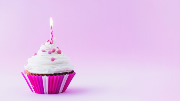 Foto magdalena del cumpleaños con la vela iluminada en fondo púrpura