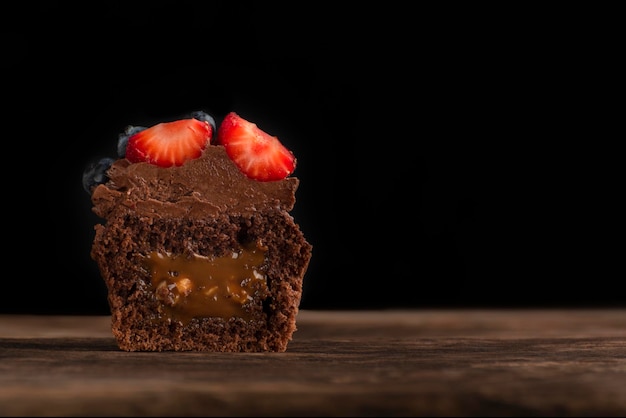 Magdalena de medio chocolate con relleno cortado en superficie de madera sobre fondo negro Muffin de chocolate fresco con bayas