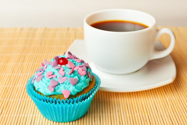 Magdalena de vainilla con crema batida y grosellas rojas y chispitas de colores con una taza de café.