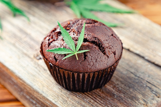 Magdalenas de chocolate con cbd de marihuana. Drogas de cáñamo de marihuana medicinal en postres de comida. Cocinar magdalenas de chocolate para hornear. Magdalena con marihuana en mesa de madera.