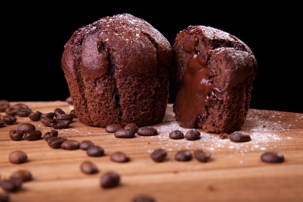 Magdalenas de chocolate con chocolate y granos de café y azúcar en una mesa de madera y fondo negro.