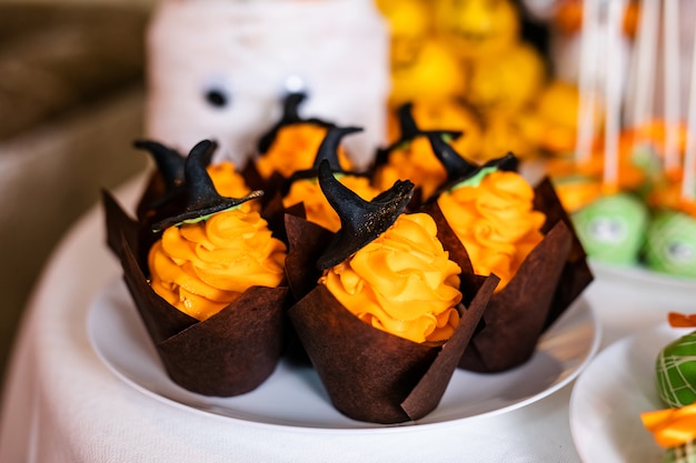 Foto magdalenas con crema de naranja y dulces sombreros negros en la barra de chocolate para la celebración de halloween