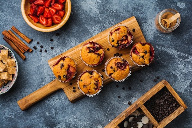 Magdalenas de cupcakes de chocolate y fresa en el antiguo soporte de madera sobre superficie gris de hormigón