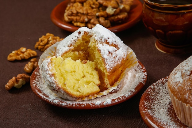 Magdalenas frescas sobre una mesa marrón con azúcar en polvo y nueces