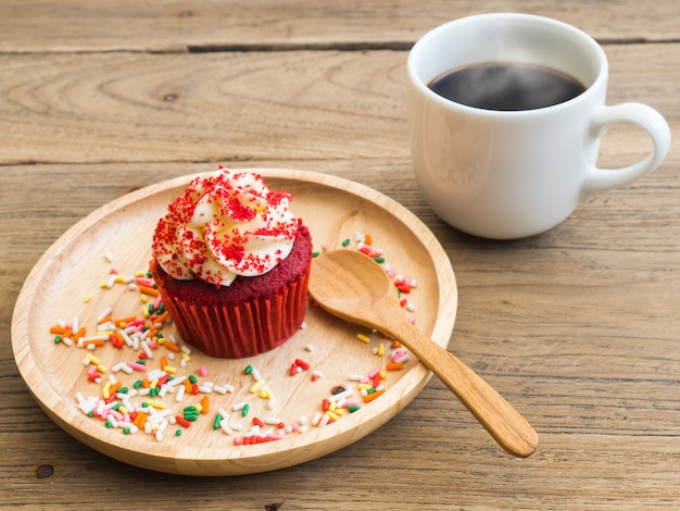 Magdalenas rojas ponen en una placa de madera. Al lado de cupcake tiene taza de café con leche.