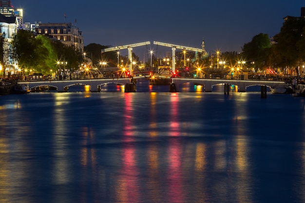 Magere Brug, Skinny Bridge, mit Nachtbeleuchtung über den Fluss Amstel im Stadtzentrum von Amsterdam, Holland, Niederlande