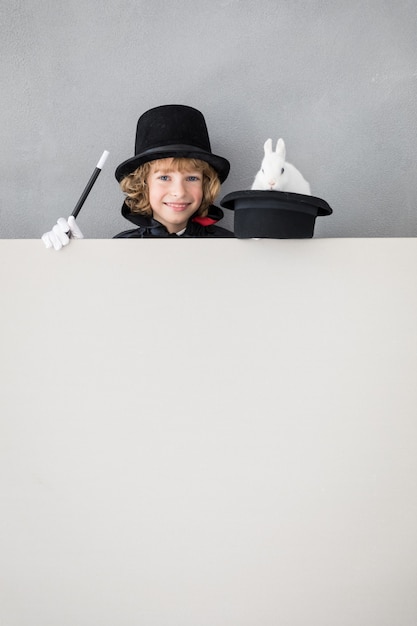 Mágico infantil com coelho se escondendo atrás de um cartaz em branco.