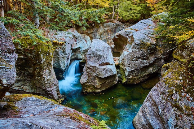Magischer Wasserfall in blaues Wasser, das durch riesige Felsen im moosigen Wald schnitzt