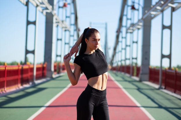 Foto magnífica chica bronceada en forma estirando las manos antes de entrenar en el parque. espacio para texto