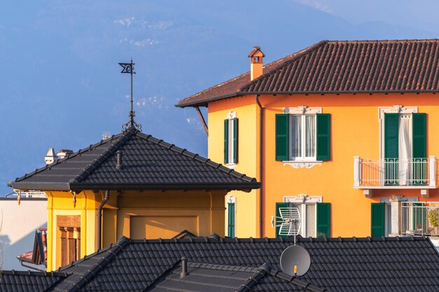 Foto magnífica fachada italiana de un edificio residencial con ventanas de persianas y techo marrón de azulejos al sol