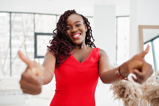 Magnífica jovem africana de vestido vermelho luxuoso em um apartamento de luxo Moda de beleza Mostre o polegar para a câmera