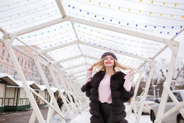 Magnífica joven modelo con maquillaje brillante, vestida con ropa de moda, posando en la calle en invierno