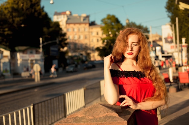 Magnífica mujer pelirroja con pelo largo y rizado posando en la avenida por la noche. Espacio para texto