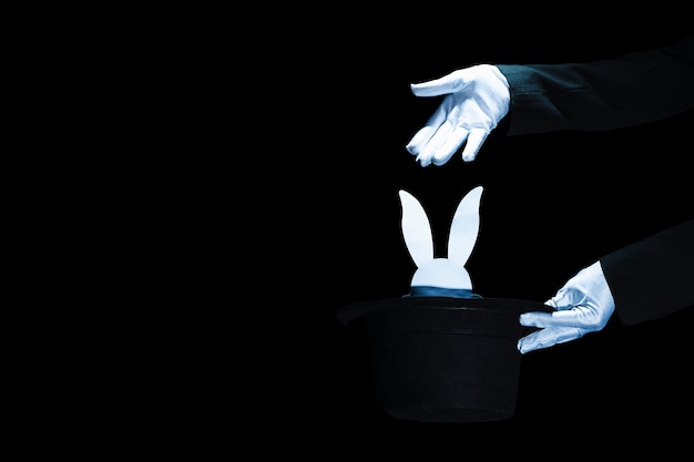 Foto mago que sostiene el sombrero de copa negro con la cabeza del conejo blanco sobre fondo negro