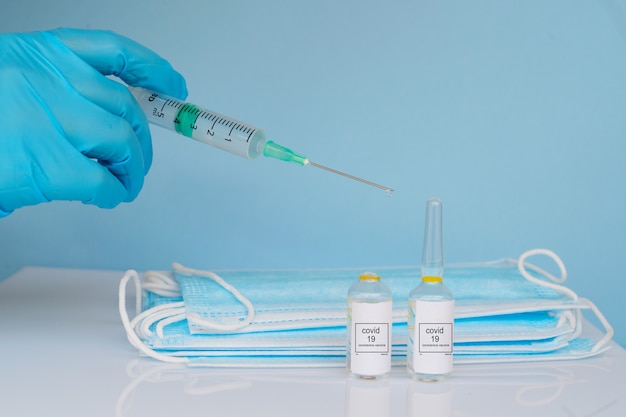 Mahing covid 16 inyección de vacuna, manos en guantes médicos con ampollas de vacuna, espacio de copia sobre fondo azul.