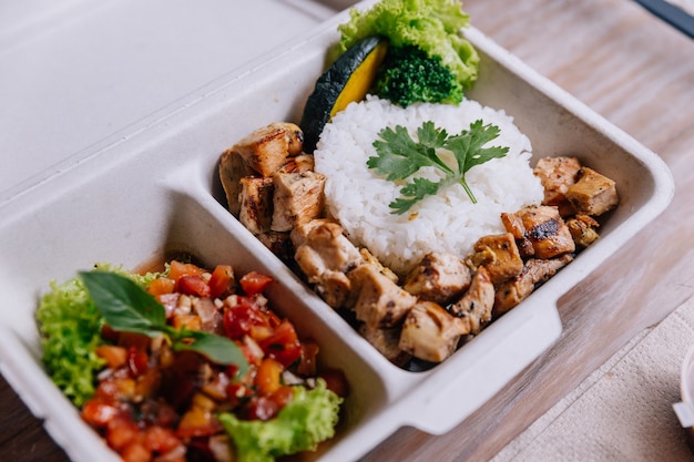 Mahlzeitkasten des sauberen Lebensmittels: Reis mit gewürfeltem Huhn diente mit Tomatensalat.