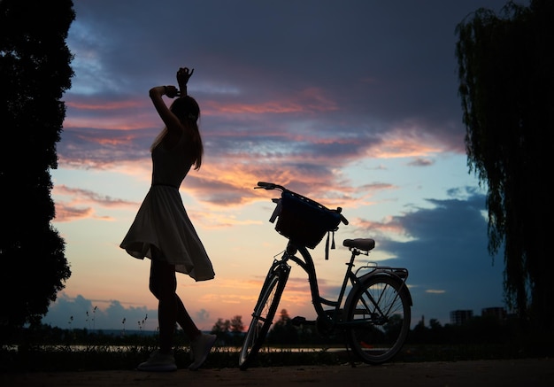 Maiden dreht sich bei Sonnenuntergang in der Nähe des Oldtimer-Fahrrads unter dem Himmel Genießen Sie im Sommer die schöne Aussicht auf den Abendhimmel