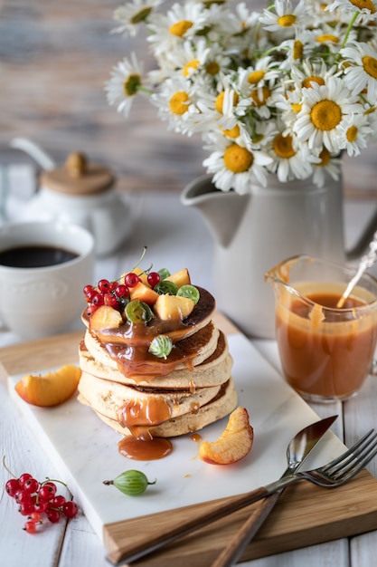 Maismehlpfannkuchen mit gesalzenem Karamell dienten mit Beeren und Früchten auf einem weißen hölzernen Hintergrund.