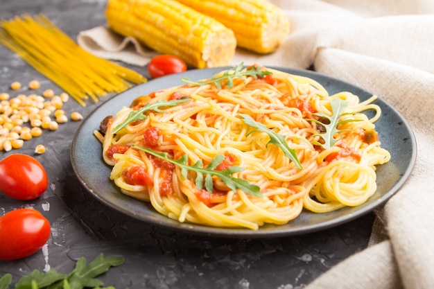 Maisnudeln mit Tomatensauce und Rucola auf schwarzem Beton.