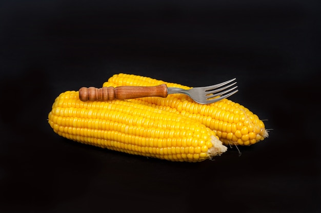 Foto maíz amarillo con tenedor sobre fondo negro