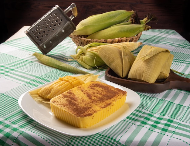 Maíz dulce Cural brasileño y maíz pamonha en la mazorca dispuestos sobre una mesa con un mantel verde y blanco fondo oscuro enfoque selectivo