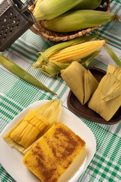 Foto maíz dulce cural brasileño y maíz pamonha en la mazorca dispuestos sobre una mesa con un mantel verde y blanco fondo oscuro enfoque selectivo