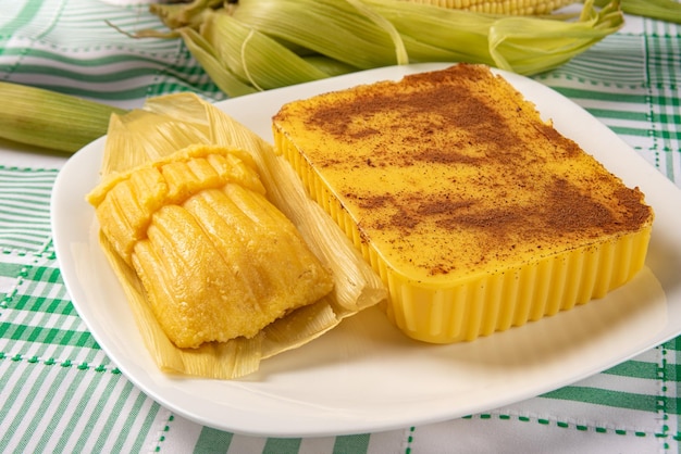 Maíz dulce Cural brasileño y maíz pamonha en la mazorca dispuestos sobre una mesa con un mantel verde y blanco fondo oscuro enfoque selectivo