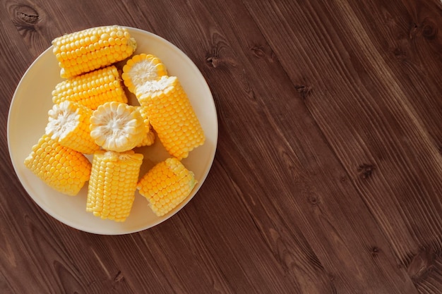 Maíz dulce fresco en un plato de cerámica beige en una mesa de madera Vista superior copia espacio para texto