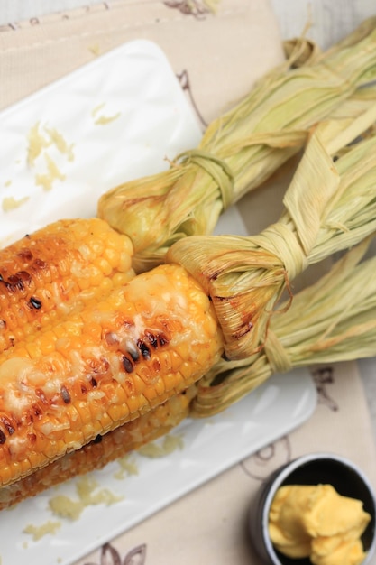 Maíz dulce a la parrilla con mantequilla y queso mozarella rallado servido en plato blanco