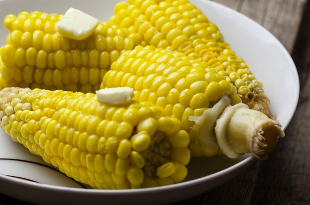 Maíz hervido con trozo de mantequilla en un plato blanco.