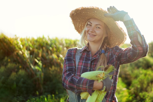 Foto maíz mujer joven agricultora sonriendo y cosechando maíz una mujer hermosa en el fondo del campo sostiene las mazorcas de maíz agricultura y horticultura