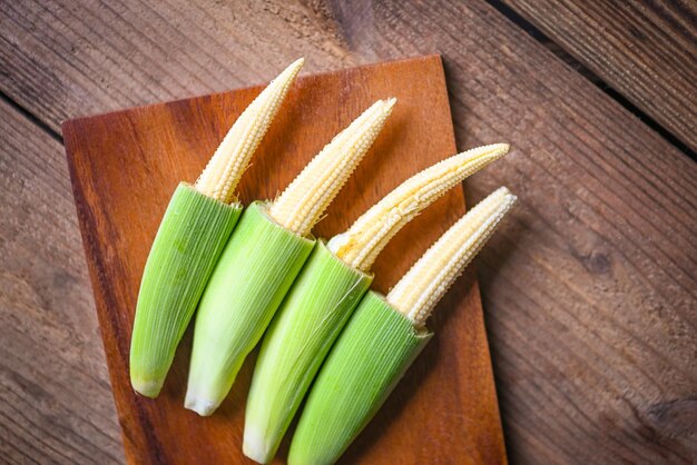 Maíz tierno sobre tabla de cortar de madera Maíz tierno fresco para cocinar alimentos saludables Cerrar maíz tierno orgánico crudo sobre fondo de madera